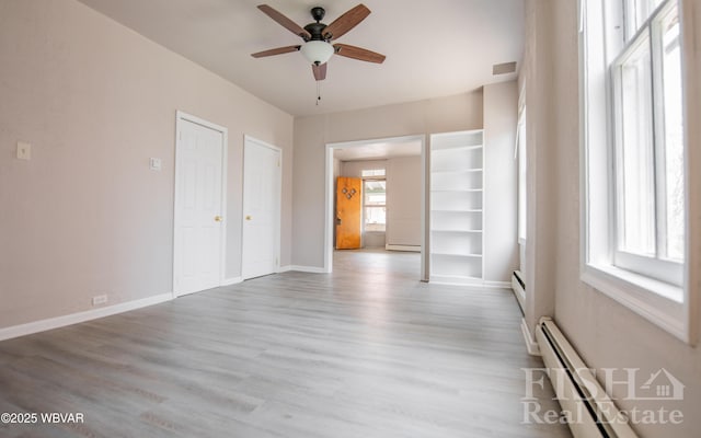 interior space with a ceiling fan, baseboards, wood finished floors, a baseboard radiator, and visible vents