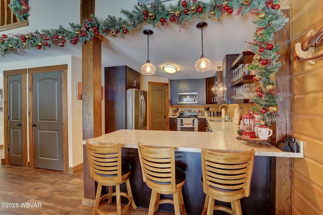 kitchen with appliances with stainless steel finishes, decorative light fixtures, a kitchen breakfast bar, light hardwood / wood-style floors, and kitchen peninsula