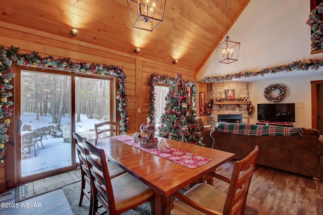 dining room featuring a stone fireplace, wood ceiling, wood-type flooring, a chandelier, and high vaulted ceiling