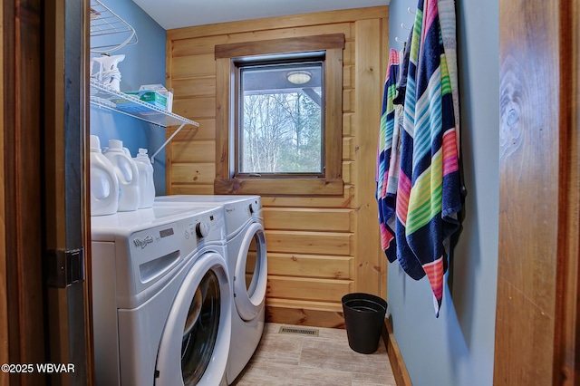 clothes washing area featuring washer and dryer and wood walls