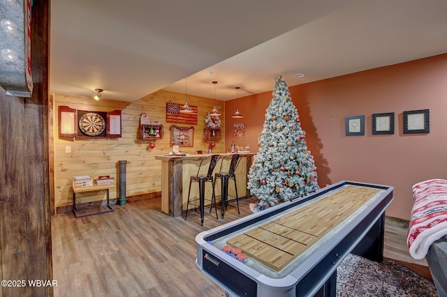 game room featuring hardwood / wood-style flooring, bar, and wood walls