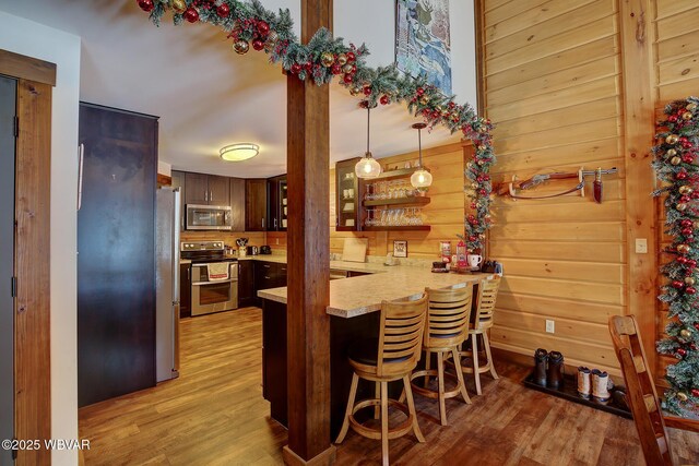 kitchen featuring a breakfast bar, wood walls, light hardwood / wood-style flooring, appliances with stainless steel finishes, and kitchen peninsula