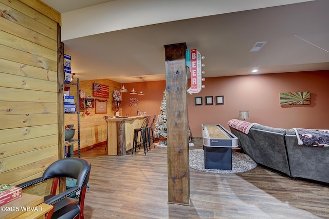 living room with hardwood / wood-style flooring, wooden walls, and indoor bar