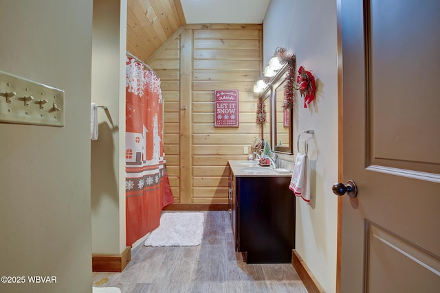 bathroom featuring wood walls, lofted ceiling, hardwood / wood-style flooring, vanity, and a shower with shower curtain