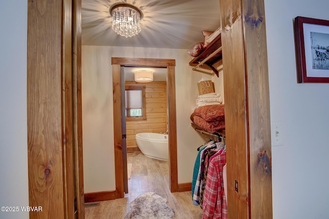 interior space with hardwood / wood-style flooring, wooden walls, a tub, and a chandelier