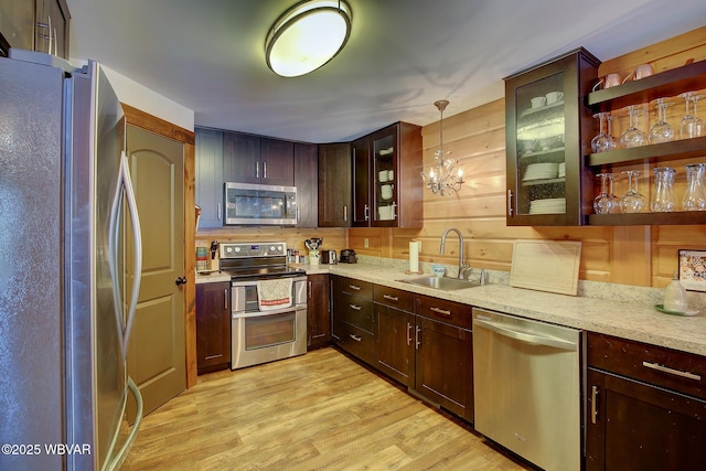 kitchen with pendant lighting, sink, light stone counters, stainless steel appliances, and light hardwood / wood-style flooring