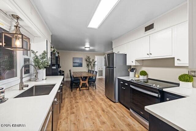 kitchen featuring sink, stainless steel appliances, light hardwood / wood-style floors, decorative light fixtures, and white cabinets