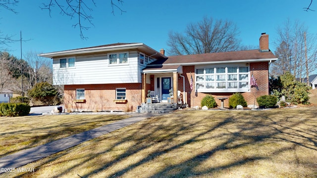 tri-level home with brick siding, a chimney, and a front yard