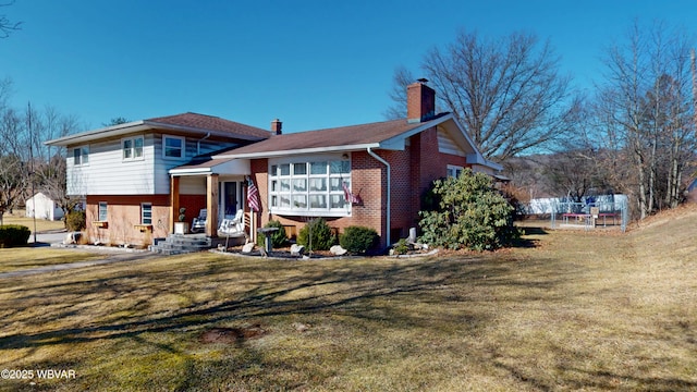 view of front of property with a front lawn, brick siding, a chimney, and fence