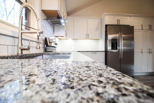 kitchen featuring decorative backsplash, stainless steel refrigerator with ice dispenser, light stone countertops, vaulted ceiling, and white cabinets