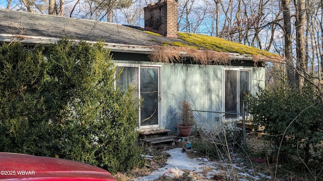 view of home's exterior with entry steps, a chimney, and roof with shingles