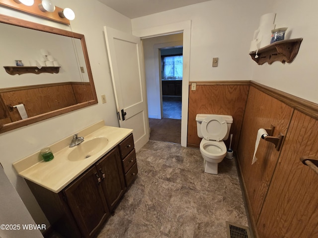 bathroom with wooden walls, visible vents, wainscoting, toilet, and vanity