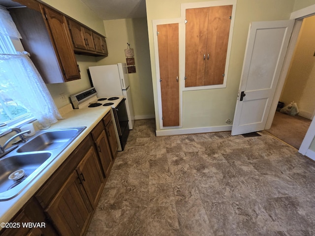 kitchen with electric stove, a sink, light countertops, and baseboards