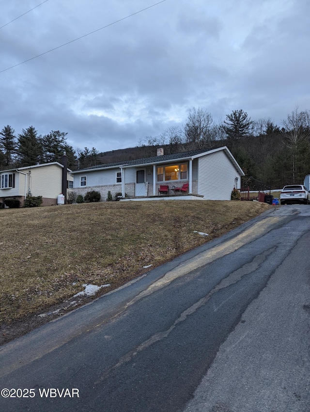 single story home featuring a front yard, covered porch, and a chimney