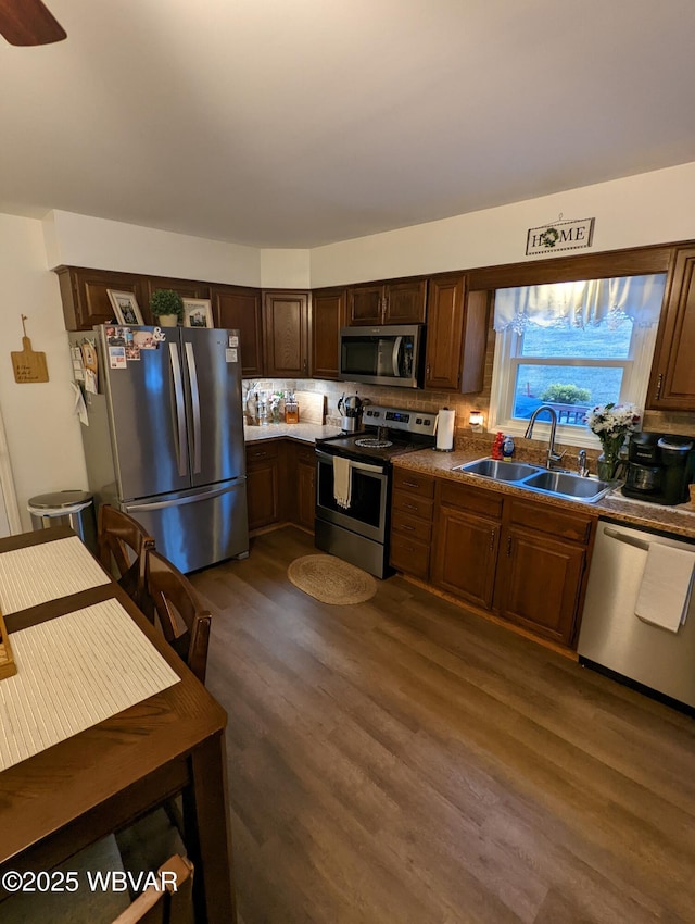 kitchen with dark wood-style flooring, dark countertops, backsplash, appliances with stainless steel finishes, and a sink