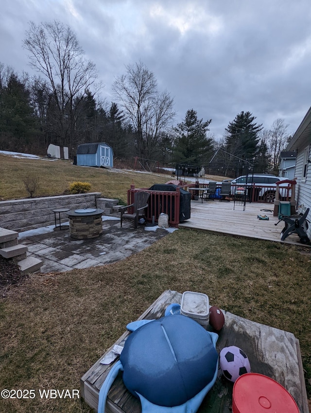 view of yard featuring a deck, a patio, an outbuilding, a fire pit, and a shed