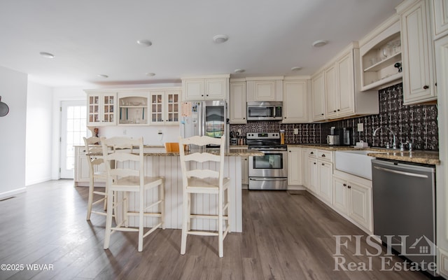 kitchen with decorative backsplash, glass insert cabinets, light stone counters, a center island, and stainless steel appliances