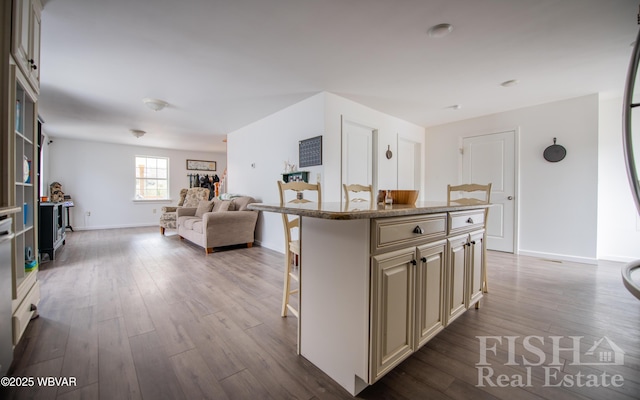 kitchen with a breakfast bar area, cream cabinets, open floor plan, a kitchen island, and light wood-type flooring