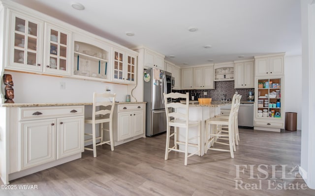 kitchen featuring stainless steel appliances, a breakfast bar area, glass insert cabinets, and light stone countertops