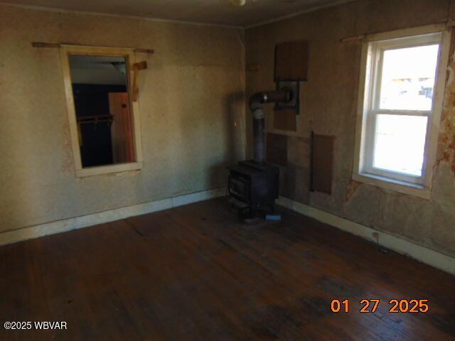 unfurnished living room featuring a healthy amount of sunlight, dark hardwood / wood-style floors, and a wood stove