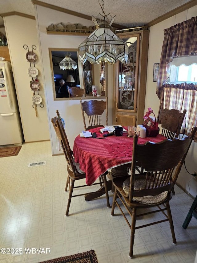 dining area with lofted ceiling, ornamental molding, and a textured ceiling