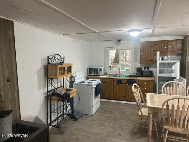 kitchen with electric stove, brown cabinets, stainless steel microwave, a sink, and wood finished floors