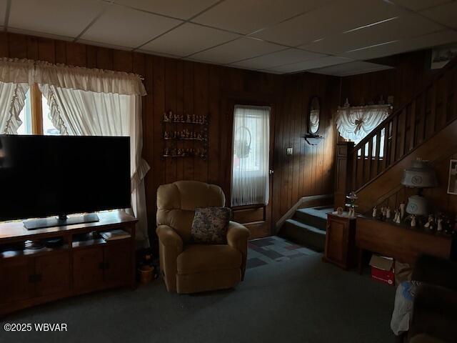 sitting room featuring a drop ceiling, wooden walls, and carpet flooring