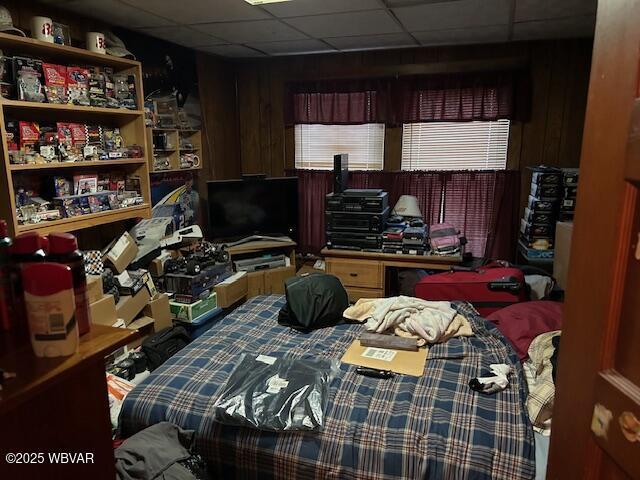 bedroom featuring a paneled ceiling and wood walls