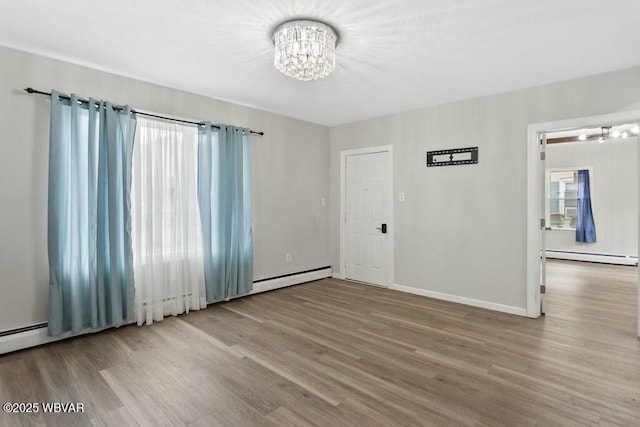 spare room with a baseboard radiator, wood finished floors, baseboards, and a notable chandelier