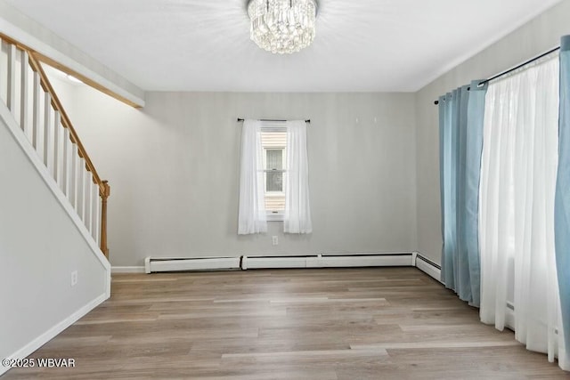 spare room with a baseboard heating unit, wood finished floors, an inviting chandelier, and stairway