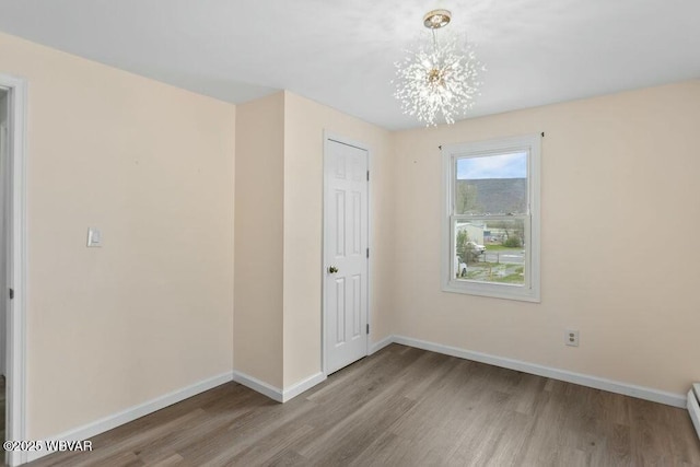 empty room with a baseboard radiator, wood finished floors, baseboards, and a notable chandelier