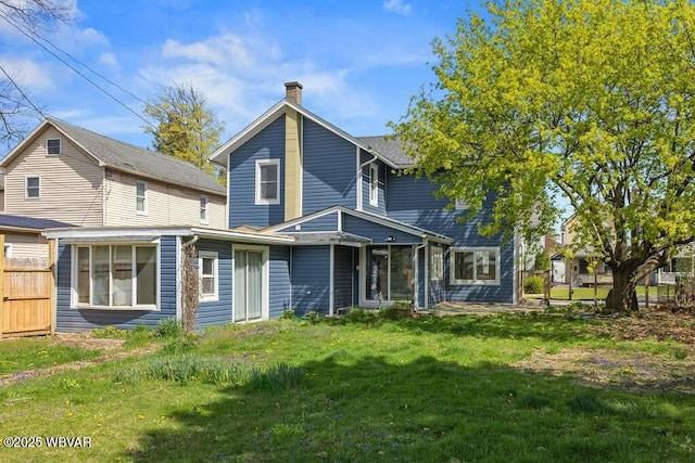 rear view of property with a lawn, a chimney, and fence