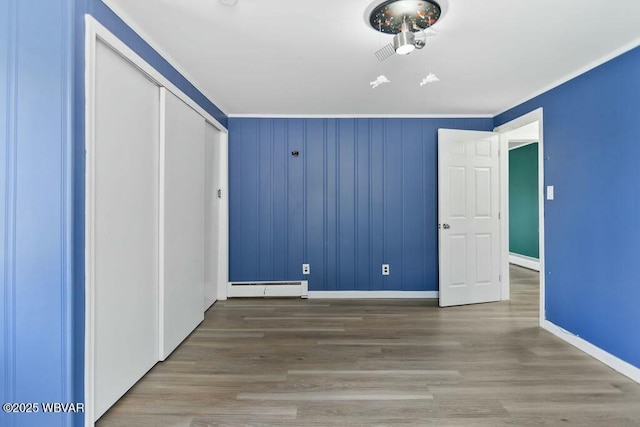 unfurnished bedroom with a baseboard heating unit, a closet, crown molding, and baseboards