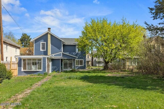 rear view of house featuring a chimney, fence, a yard, and a sunroom