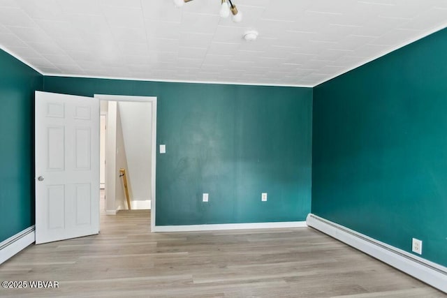 spare room featuring a baseboard radiator, wood finished floors, and baseboards
