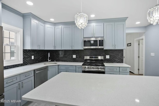 kitchen featuring stainless steel appliances, light countertops, a sink, and an inviting chandelier