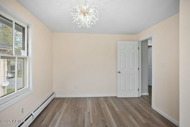 unfurnished room featuring a baseboard heating unit, wood finished floors, baseboards, and a notable chandelier