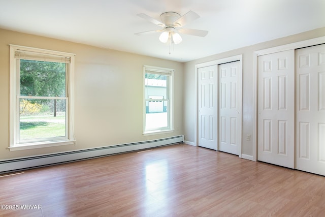 unfurnished bedroom featuring baseboard heating, ceiling fan, light wood-style floors, and two closets