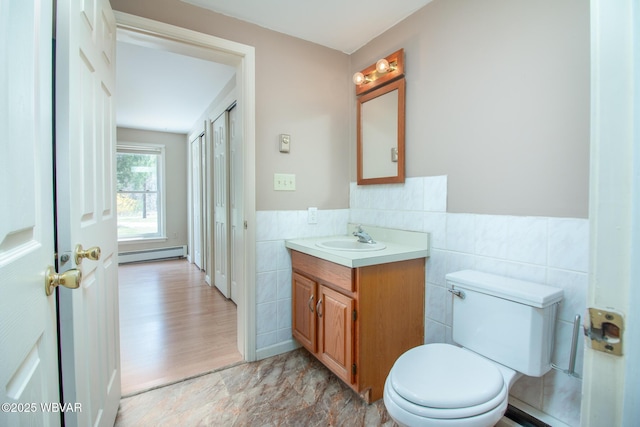 bathroom featuring wainscoting, tile walls, baseboard heating, toilet, and vanity