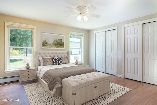 bedroom with wood finished floors, multiple closets, a baseboard heating unit, and multiple windows