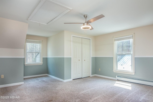 unfurnished bedroom with a closet, baseboard heating, attic access, carpet flooring, and baseboards