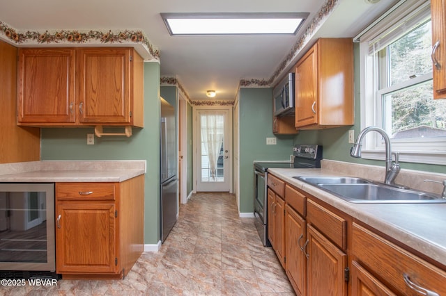 kitchen with a sink, stainless steel appliances, light countertops, wine cooler, and brown cabinetry
