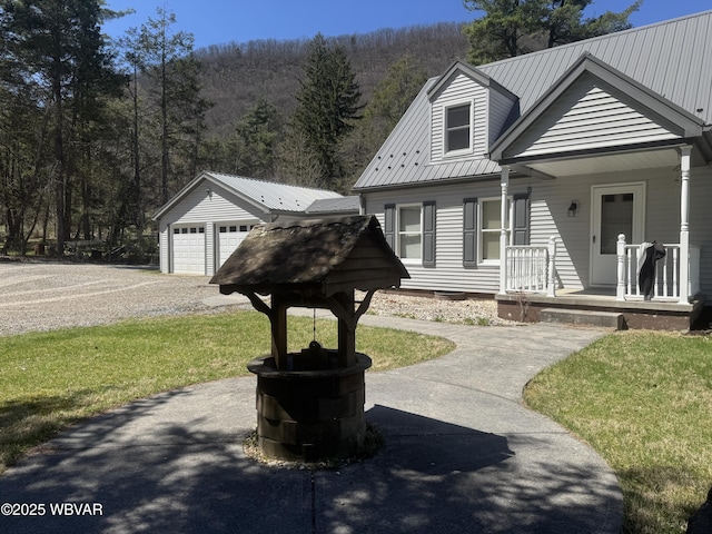 new england style home featuring a porch, an outbuilding, metal roof, a garage, and a front yard