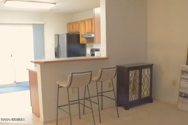 kitchen with stainless steel refrigerator with ice dispenser, a wealth of natural light, a kitchen bar, and kitchen peninsula