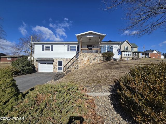 view of front of house featuring stairway, a porch, an attached garage, stone siding, and aphalt driveway