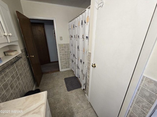 full bath featuring a shower with shower curtain, a wainscoted wall, tile walls, and tile patterned flooring