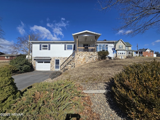 view of front of home with stairway, a porch, a garage, stone siding, and aphalt driveway