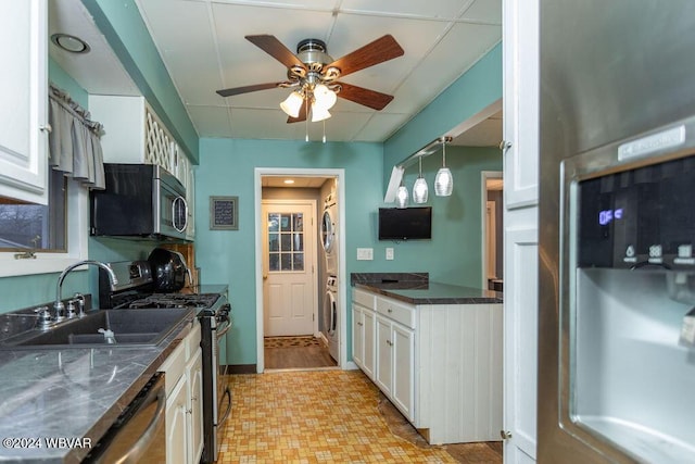 kitchen with pendant lighting, stacked washer and clothes dryer, white cabinets, sink, and appliances with stainless steel finishes