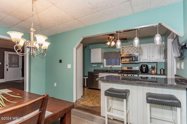 kitchen with kitchen peninsula, ceiling fan with notable chandelier, stainless steel appliances, hanging light fixtures, and a breakfast bar area