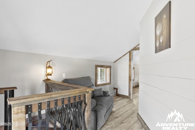 bedroom featuring light wood finished floors, wooden walls, a baseboard heating unit, and vaulted ceiling